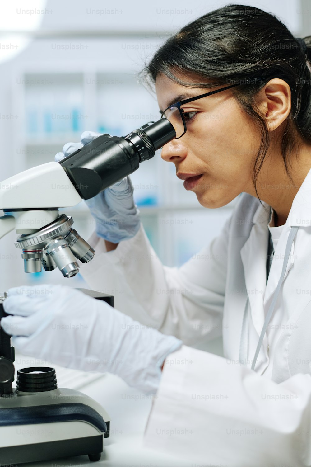 Microbiologista ou virologista do sexo feminino sério usando microscópio em laboratório enquanto faz pesquisa científica ou experimento