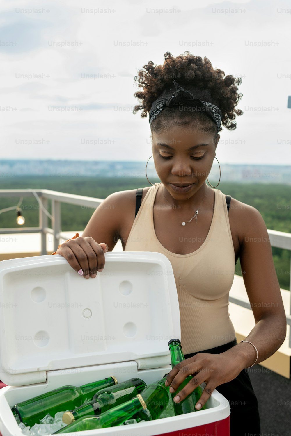 Young pretty female taking bottle of beer out of box with ice cubes in outdoor cafe at party