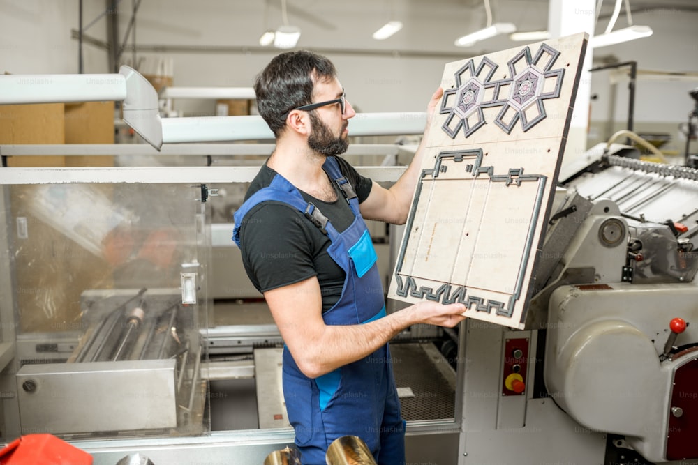 Trabajador de pie con el cliché para cortar cajas en la fabricación de impresión vintage