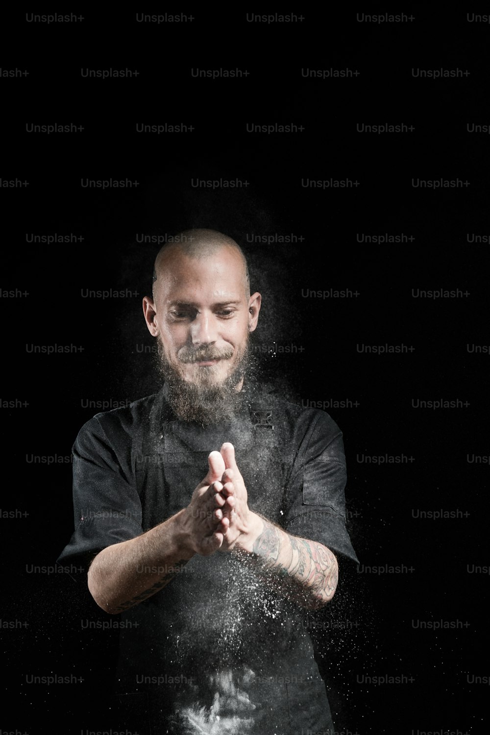 Portrait of chef in studio on black, clapping hands with flour, making fresh dough,