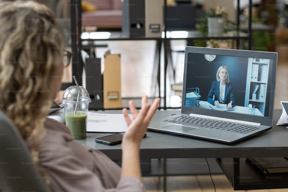 Vista trasera de una empresaria hablando con su colega en la pantalla de la computadora portátil, discuten el trabajo durante la conferencia en línea en la oficina
