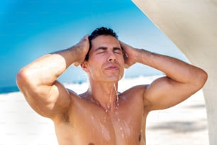 Homme musclé nu prenant une douche avec de l’eau froide après avoir pris un bain de soleil à la plage par temps chaud