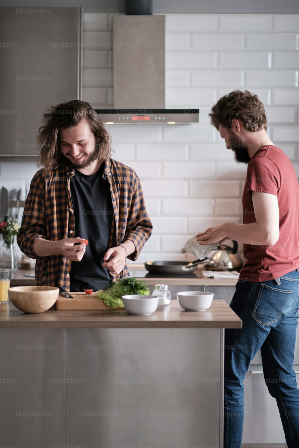 Retrato de dois homens em pé na cozinha, cozinhando, fazendo salada. Um homem está de frente para a câmera, outro virou as costas