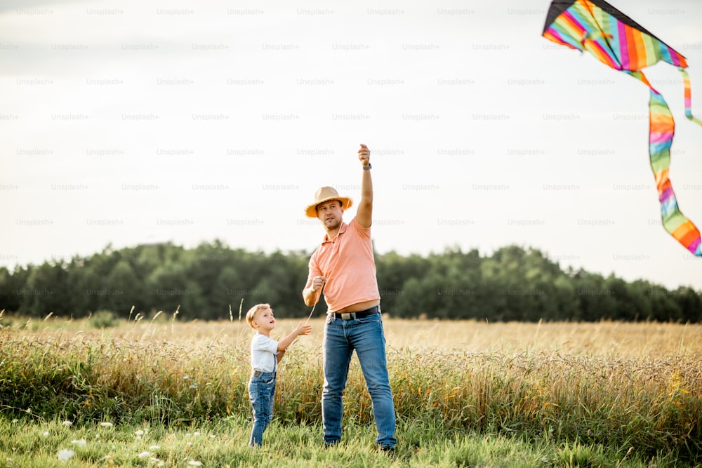 Padre con hijo lanzando coloridas cometas aéreas en el campo durante la puesta de sol. Concepto de una familia feliz divirtiéndose durante la actividad de verano