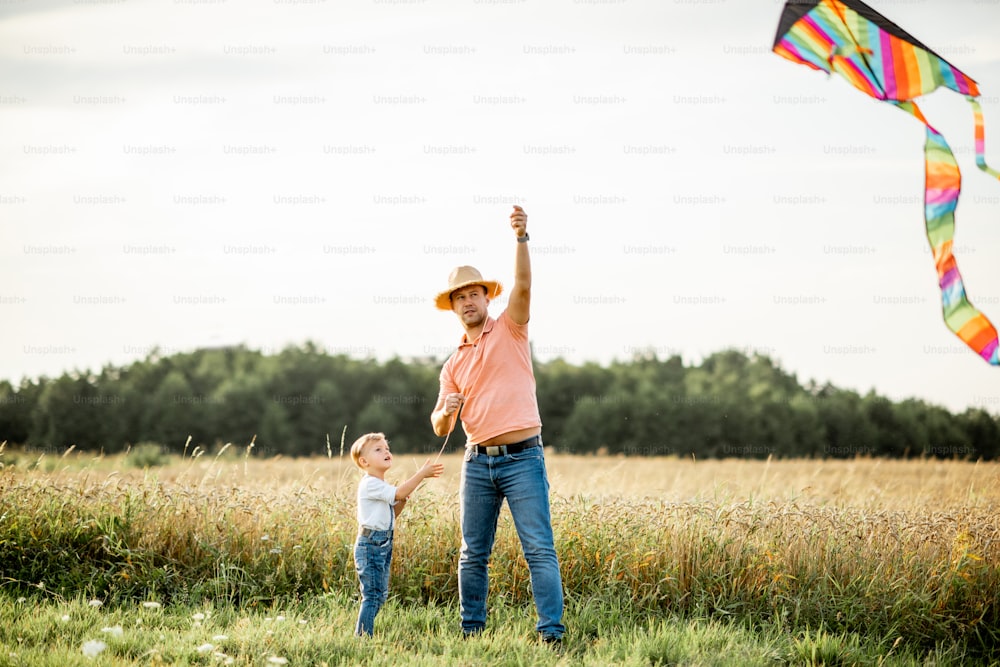 Father with son launching colorful air kite on the field during the sunset. Concept of a happy family having fun during the summer activity