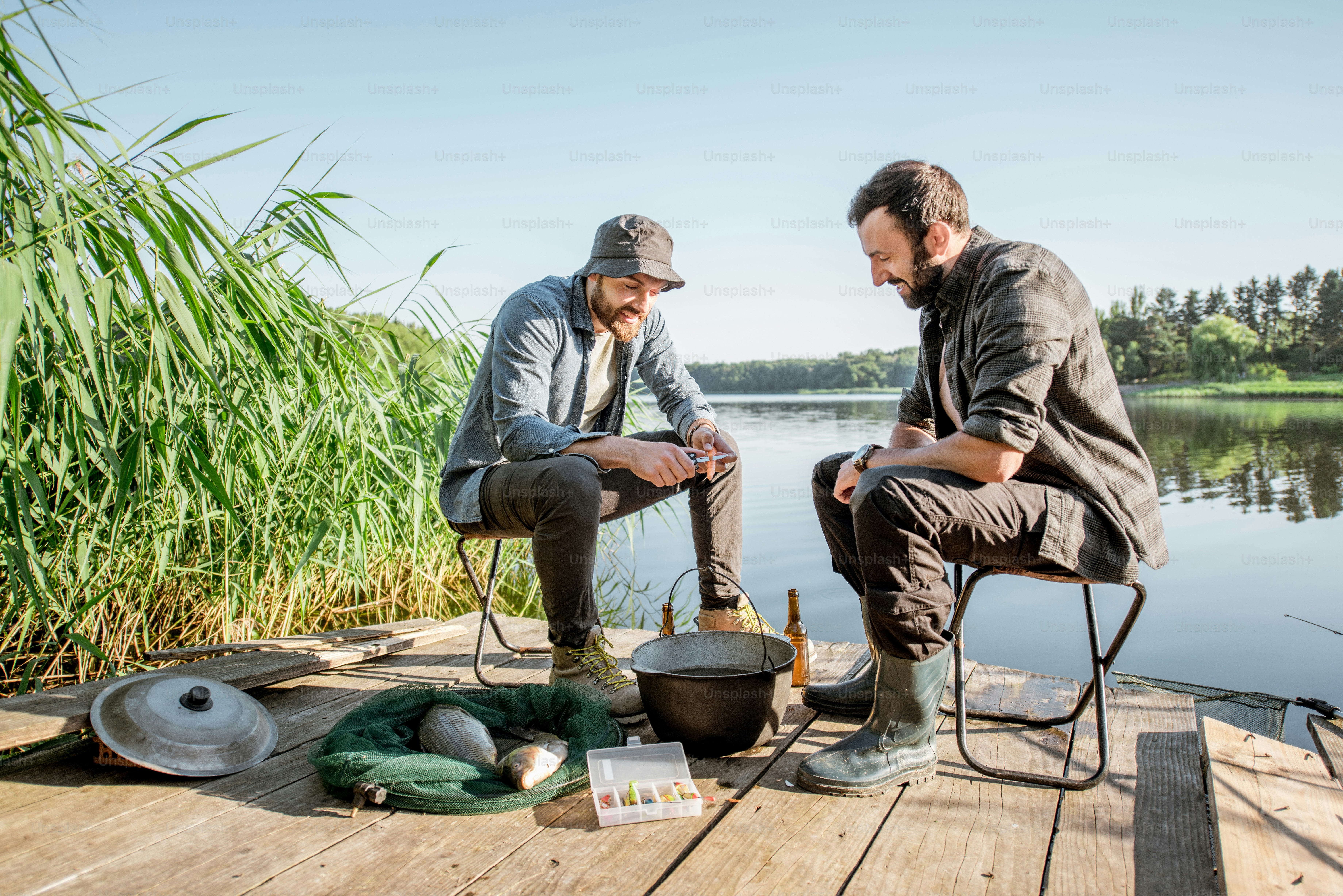 Two fishermen relaxing during the picnic on the wooden pier near the lake in the morning