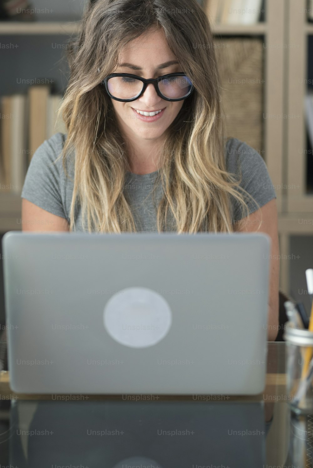 La donna graziosa con gli occhiali gli occhiali lavora a casa sul computer portatile - persone femminili in smart working alla scrivania dell'ufficio che guardano il monitor - concetto di stile di vita freelance professionale e moderno