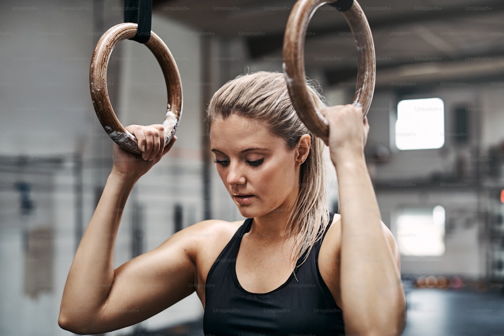 Une jeune femme en tenue de sport en forme a l’air concentrée tout en s’entraînant sur des anneaux lors d’une séance d’exercice dans un gymnase