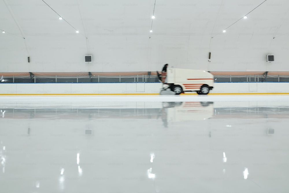 대형 스포츠 센터 내부에서 하키 또는 스케이트를 준비하면서 아이스 링크를 따라 움직이는 흰색 트럭 또는 얼음 평탄화 기계