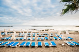 Niemand am Strand un leere Kunden Sommergeschäft. Viele Sitze und geschlossene Sonnenschirme im tropischen Sommerplatz. Urlaubs- und Entspannungskonzept mit Sitzhintergrund und ruhigem Meer
