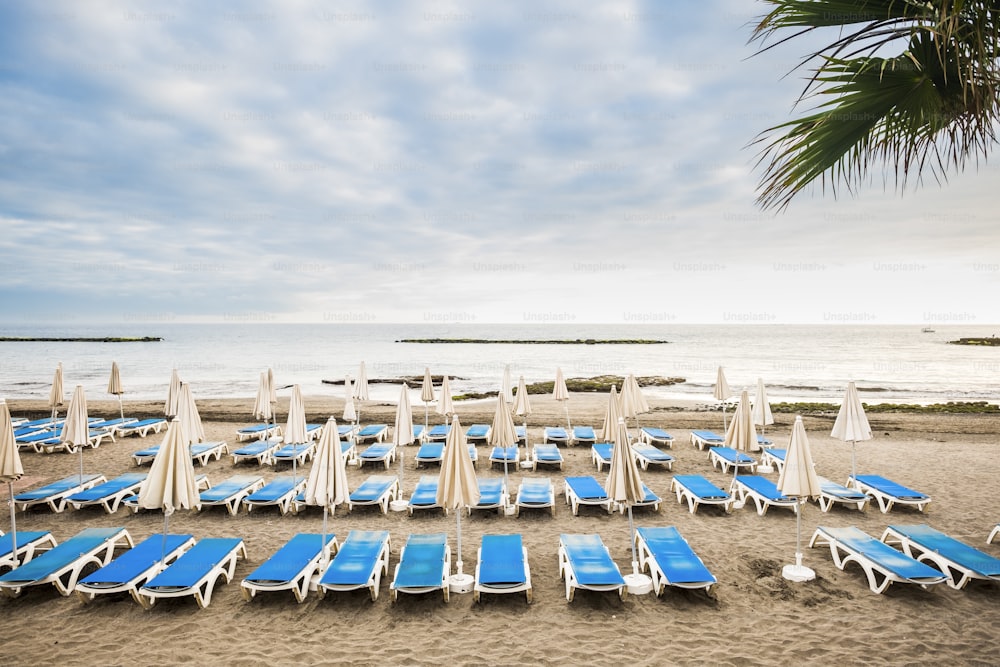 Nessuno in spiaggia un vuoto clienti affari estivi. Molti posti a sedere e ombrelloni chiusi in luogo estivo tropicale. Concetto di vacanza e relax con sfondo di sedili e oceano tranquillo