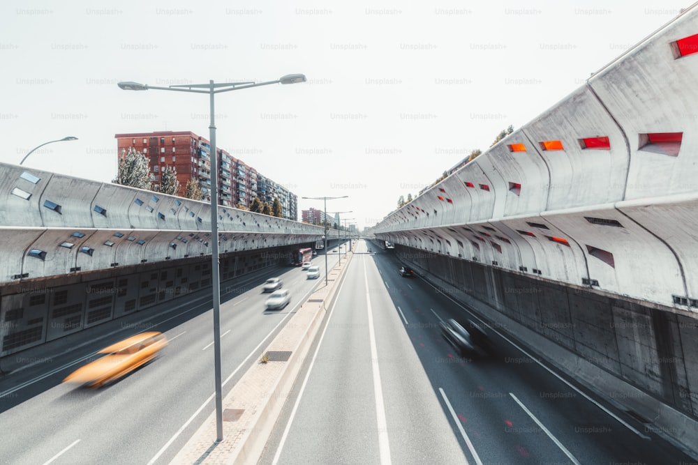 Eine moderne Autobahn in der Aussparung, die sich bis zum Fluchtpunkt erstreckt, im Zentrum von Barcelona, Spanien, mit schalldichten Betonwänden, Langzeitbelichtung, mehreren verschwommenen Autos und dem Bus, sonniger Sommertag