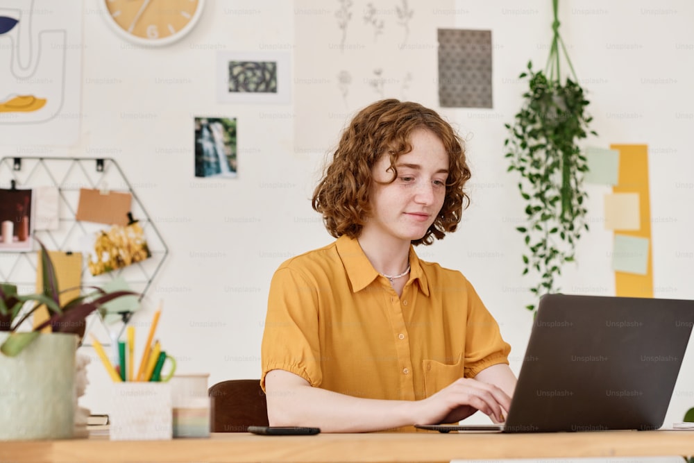 Jovem empresária confiante olhando através de dados na tela do laptop enquanto sentada no local de trabalho na sala de estar