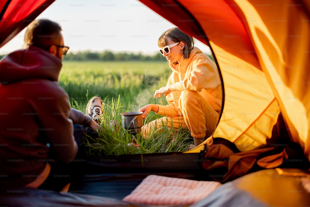Junges Paar bereitet Essen zu, während es mit Zelt in der Natur reist. Mann und Frau verbringen den Sommer auf dem Campingplatz. Blick durch die Zelttür