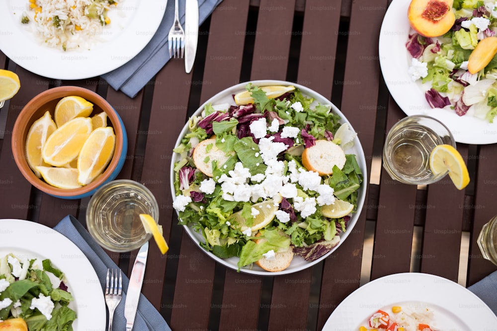 Above view background image of delicious light meal on wooden table: salads and fruits in elegant bowls surrounded by glasses with refreshing lemonade