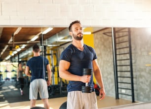 Muscular serious man in sportswear holding dumbbell. In background his reflection in mirror.