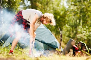 Young scout putting stick into ground while preparing place for cooking food over campfire