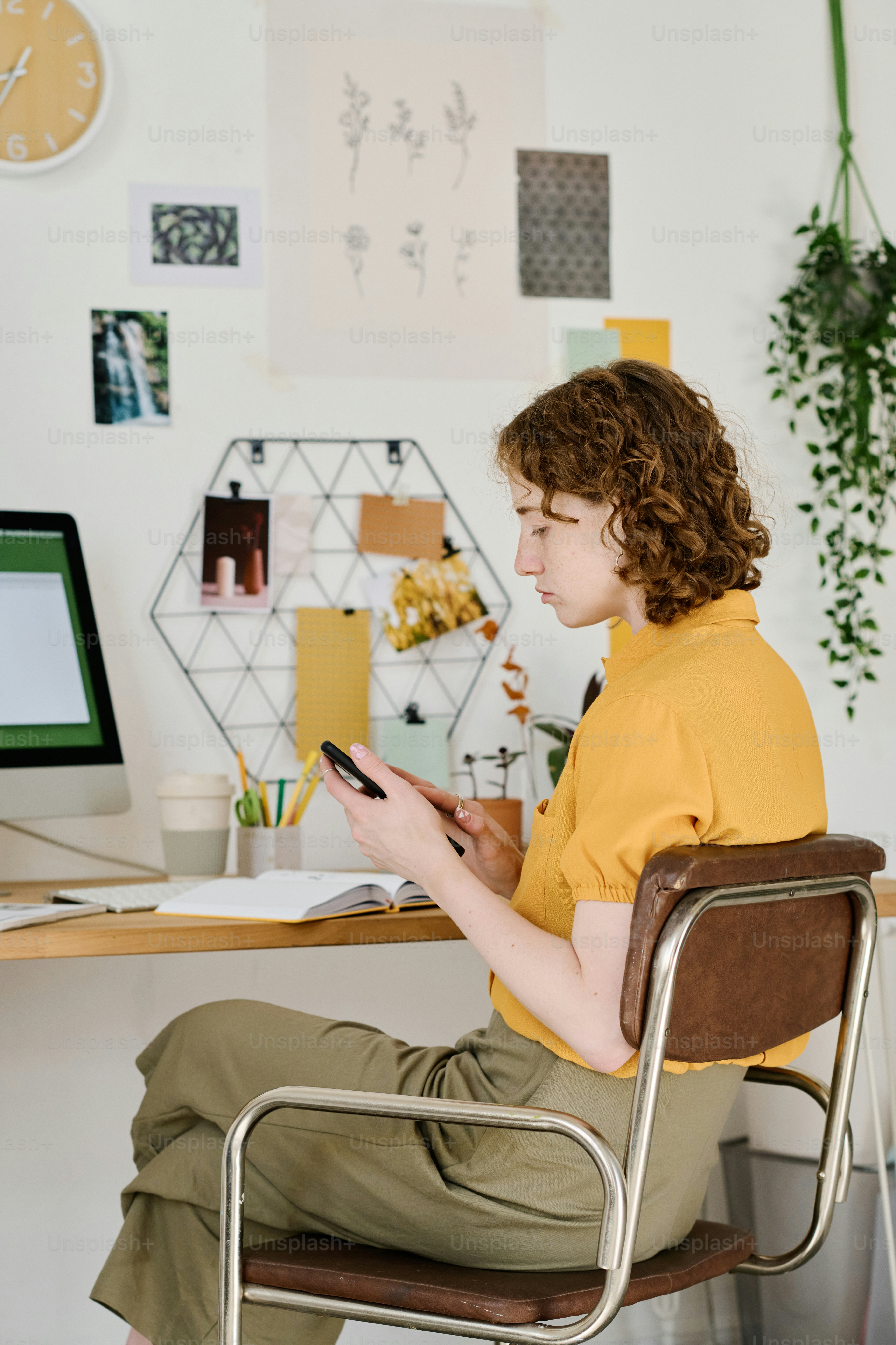 Giovane studentessa o libera professionista con messaggi di testo sul telefono cellulare o guardando informazioni online mentre è seduta sul posto di lavoro a casa