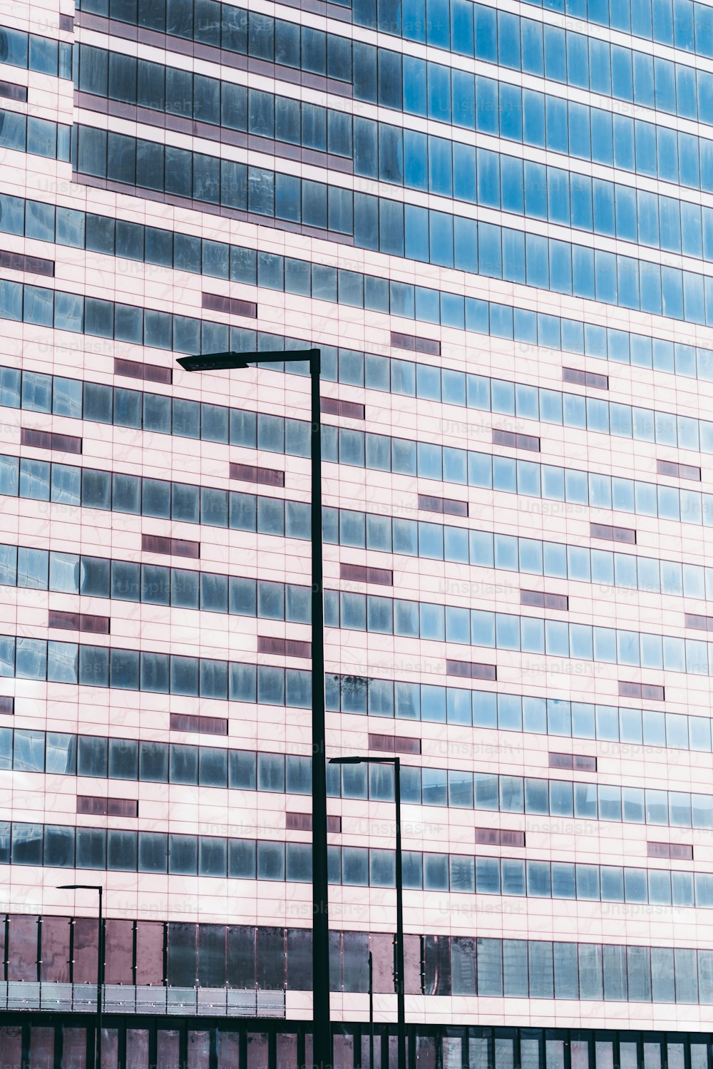 Fachada de vidro de um arranha-céu de escritórios em construção: muitas janelas empoeiradas de escritórios vazios, azulejos, lanternas; tonalidade da cor para o rosa, céu azul refletindo no vidro