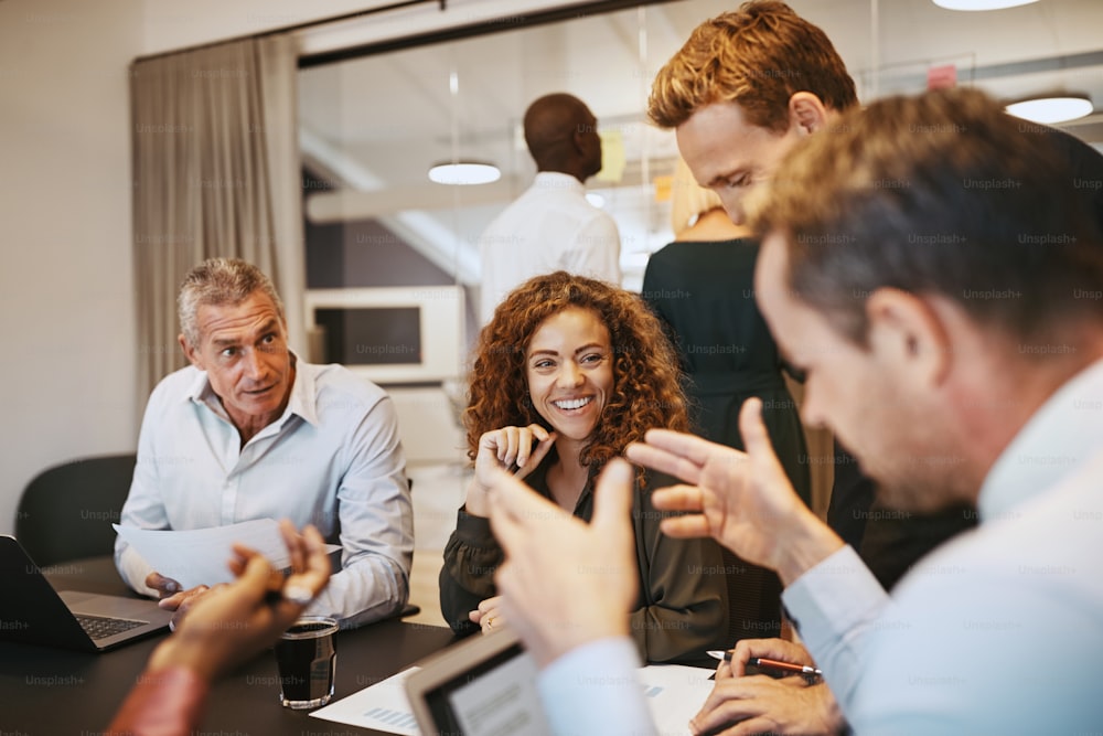 Grupo diversificado de empresários sorridentes conversando durante uma reunião em torno de uma mesa em uma sala de reuniões do escritório