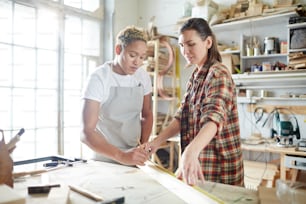 Two young females measuring wooden plank in contemporary workshop