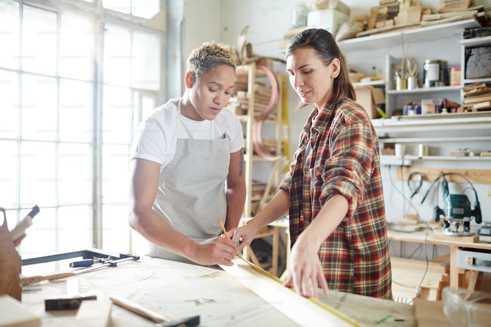 Dos mujeres jóvenes midiendo tablones de madera en un taller contemporáneo
