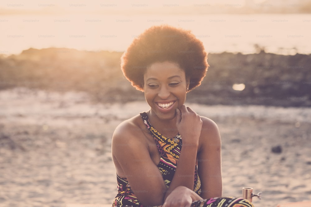 nice beautiful young model lady female black race african afro with nice hair stay sit down and smile enjoy the life at sunset with sun in backlight on the beach for vacation
