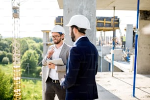 주거용 건물 건설 과정을 감독하는 두 명의 엔지니어 또는 건축가가 야외 구조물에 서 있습니다.