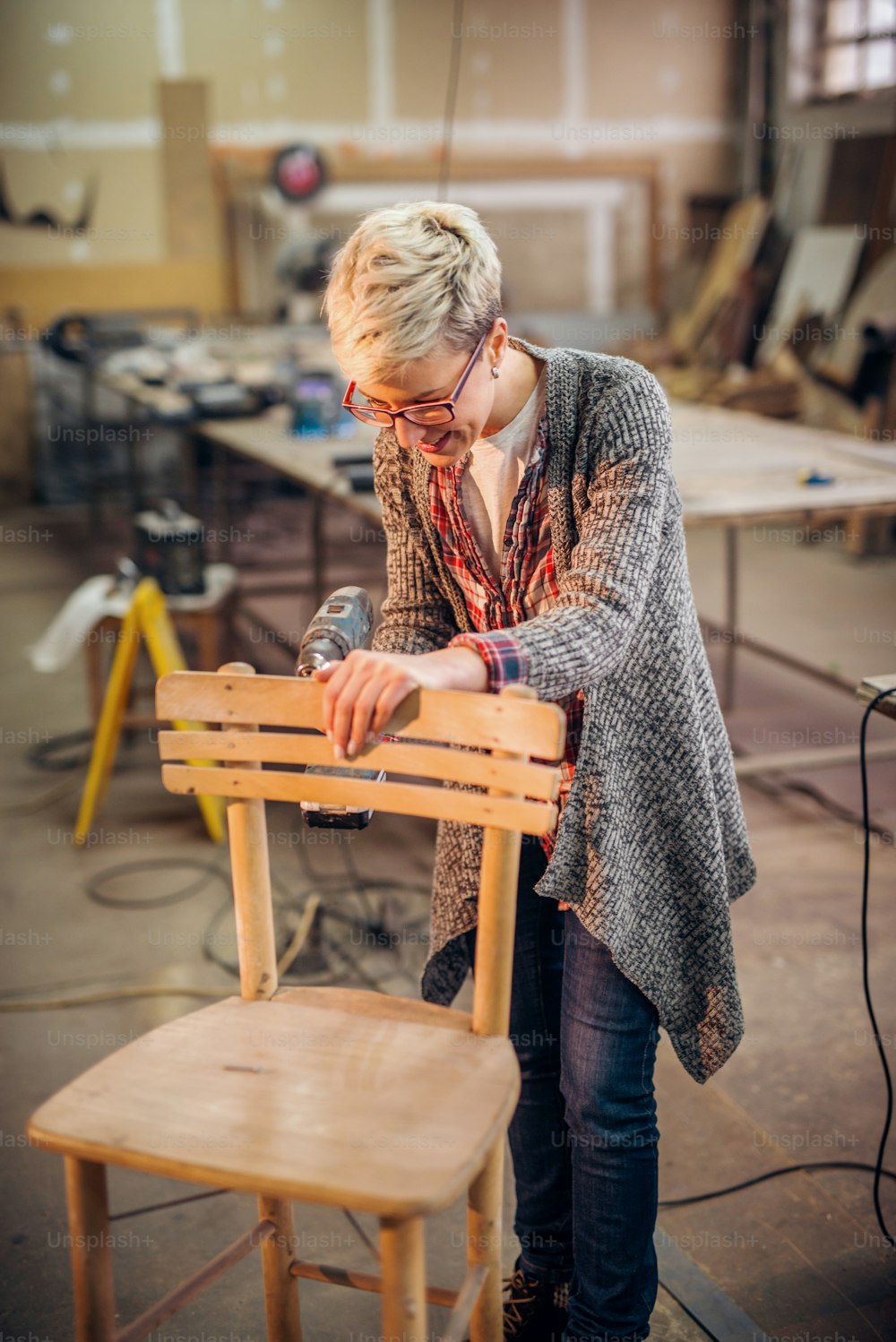 의자를 만들기 위해 드릴을 사용하는 여성 목수. 워크샵 인테리어.