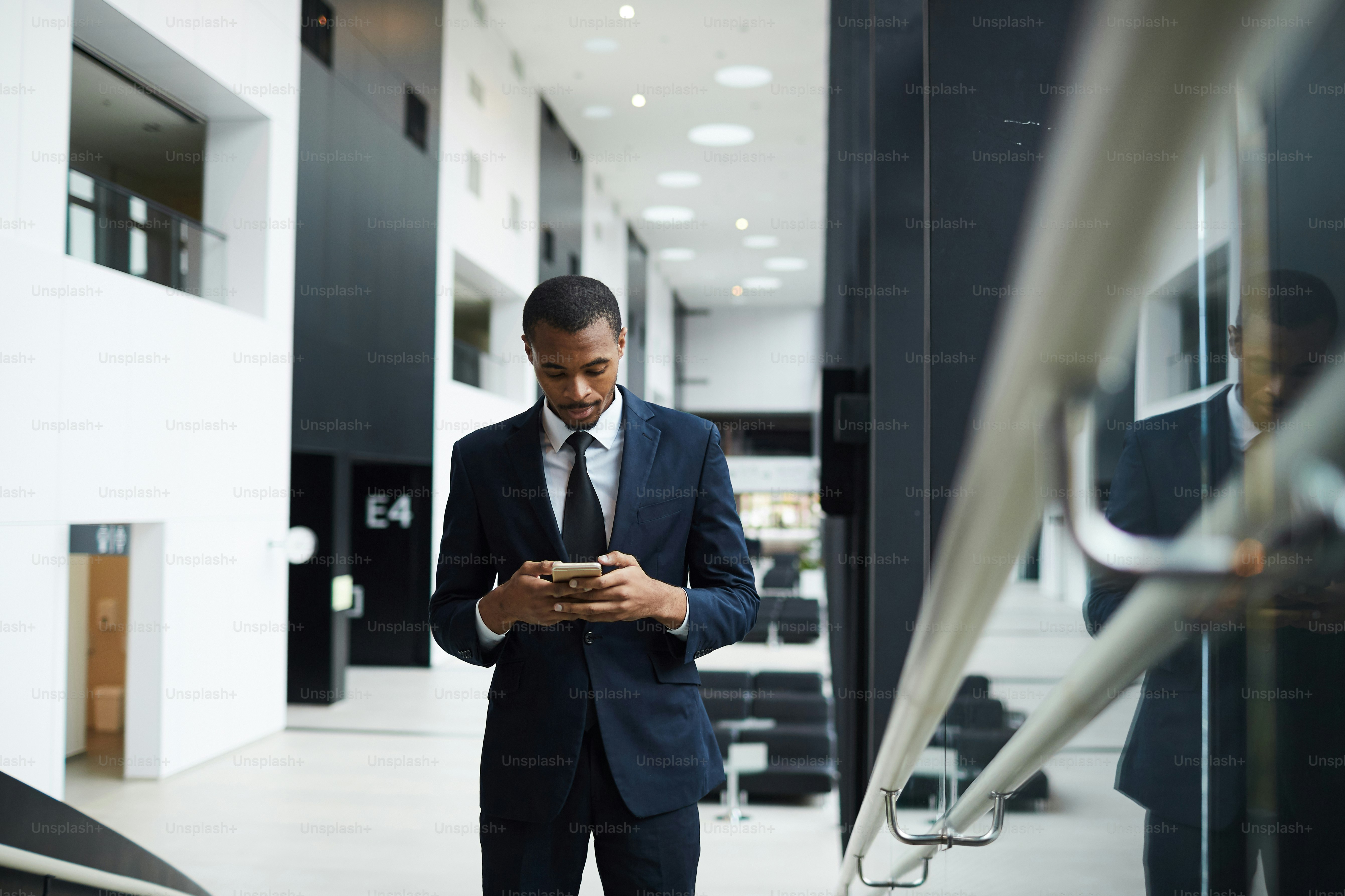 Young elegant agent in formalwear reading message or notification in smartphone inside business center