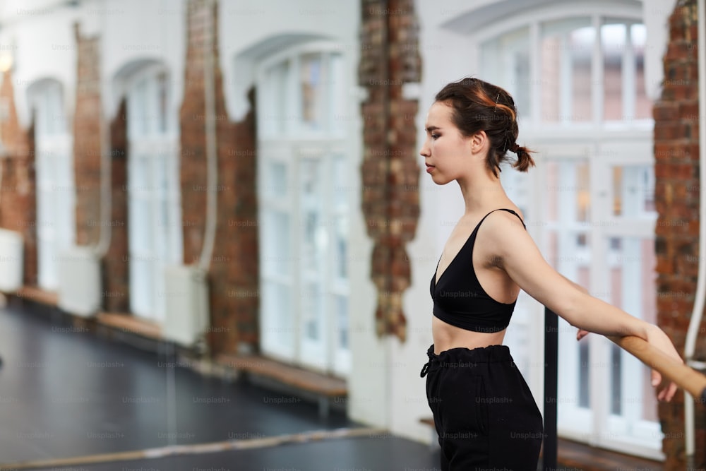 Fit and sporty girl in activewear standing by gymnastic bar while exercising in studio