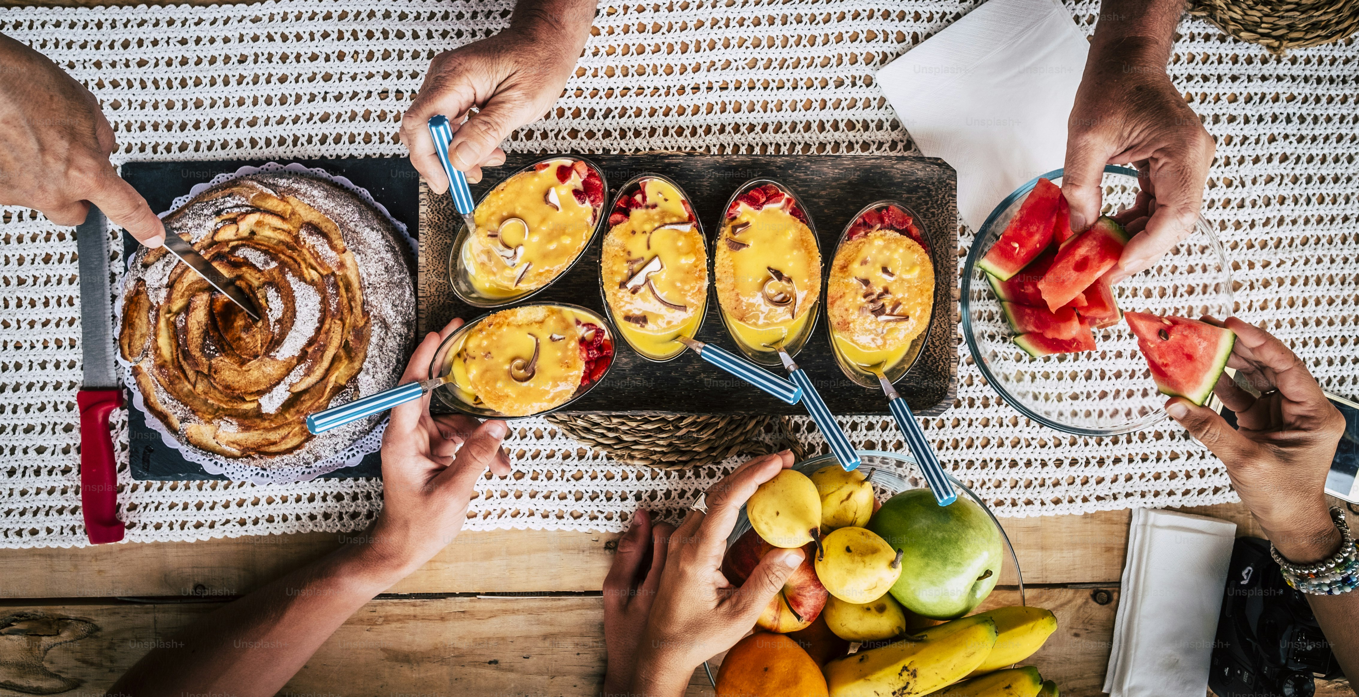 Appetizer table with food viewed from above with people friendship together concept eating and celebrating - wooden background and dessert cakes and hands taking things