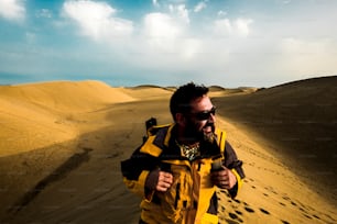 Homens de meia-idade caminham e exploram o deserto e as dunas de areia amarela com um céu azul ao fundo. sorriso e felicidade para as pessoas amam o ar livre e as aventuras. férias alternativas e estilo de vida