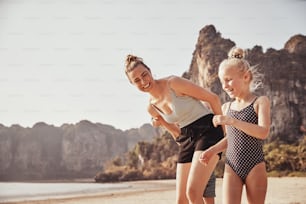 Mother and her two small children laughing while running together along a sandy beach during summer vacation
