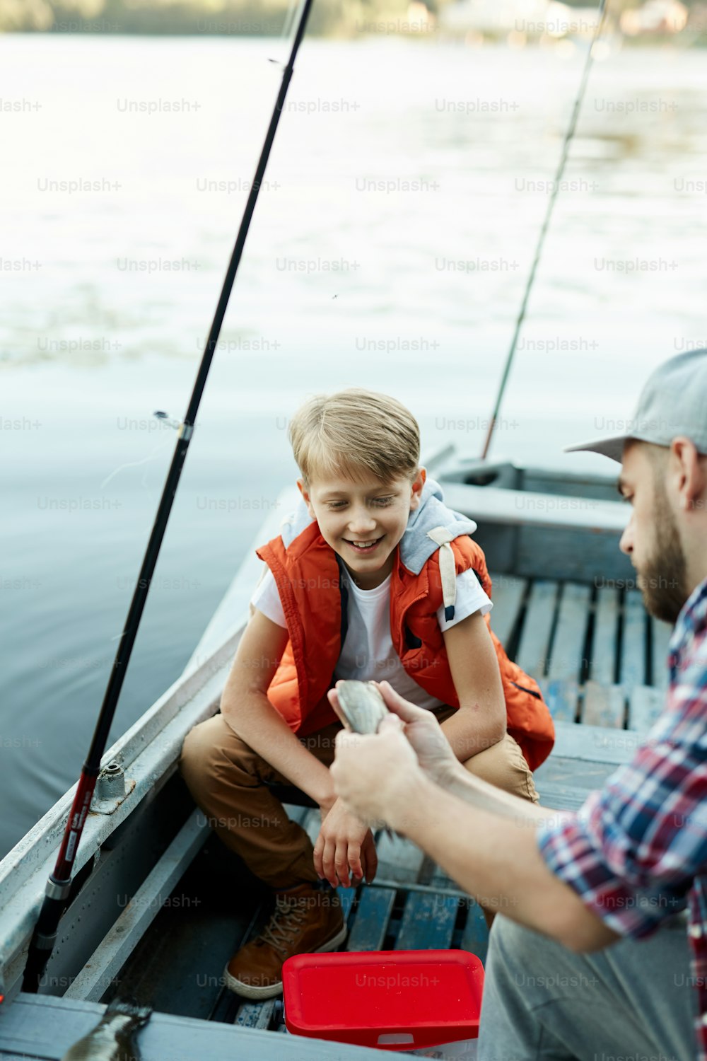 Giovane che mostra il pesce di suo figlio e indica il suo aspetto durante la loro conversazione in barca