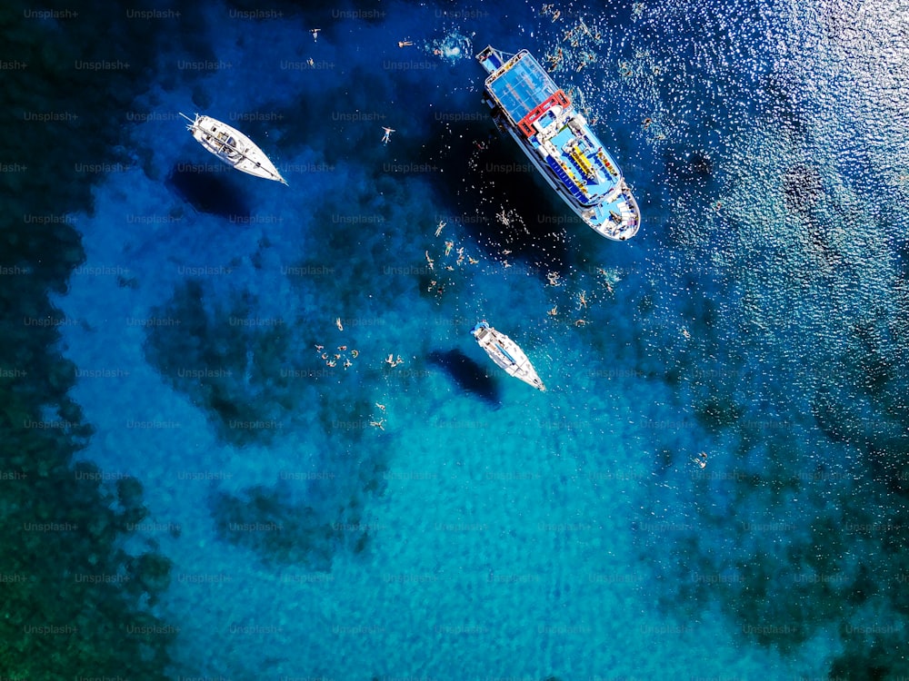 Aerial shot of beautiful blue lagoon at hot summer day with sailing boat. Top view of people are swimming around the boat.