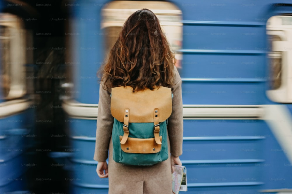 Mujer joven rizada pelirroja viajera con mochila y mapa en la estación de metro frente al tren