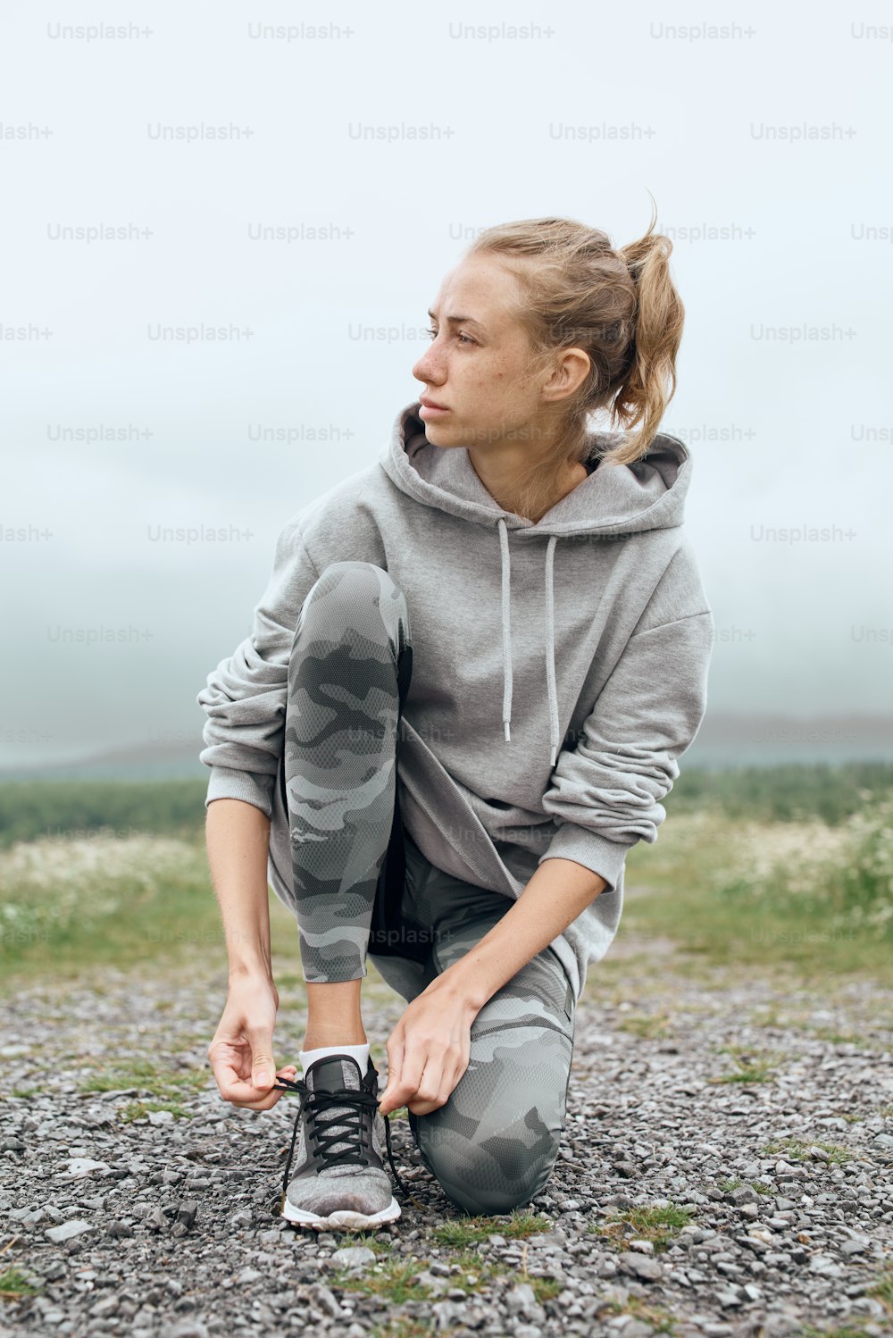 Mid age woman tying shoelaces , getting ready for work out outdoor, she is at the country road with scenic view, looking away