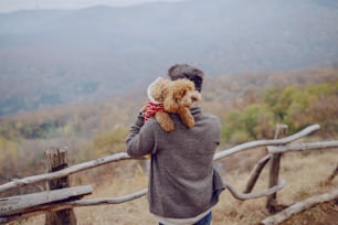 Attractive mixed race man holding his loving dog while standing in nature at fall.