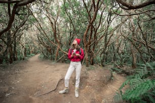 Mulher vestida casualmente na camisa vermelha e chapéu caminhando com mochila na bela floresta tropical, viajando na ilha de Tenerife, Spain
