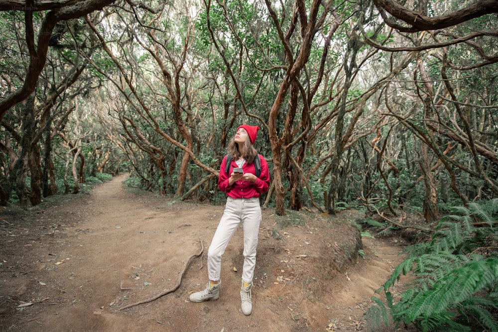 Mulher vestida casualmente na camisa vermelha e chapéu caminhando com mochila na bela floresta tropical, viajando na ilha de Tenerife, Spain
