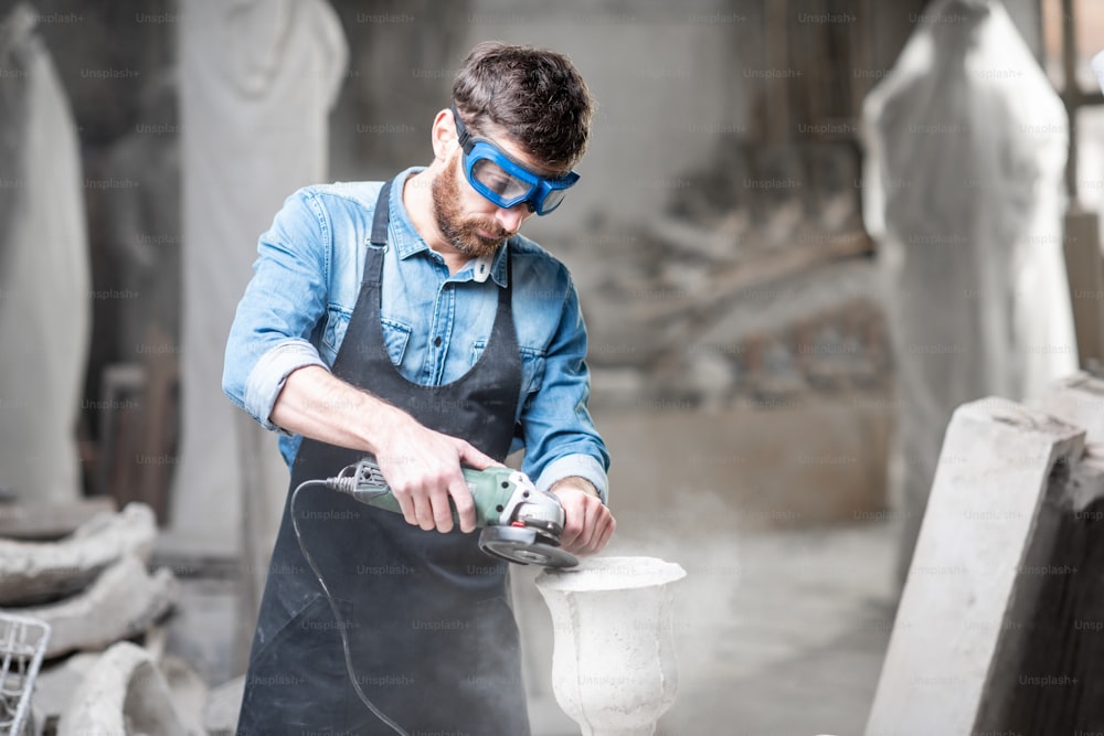 Escultor en utensilios de trabajo moliendo jarrón de piedra en el espacio de trabajo en el antiguo estudio atmosférico
