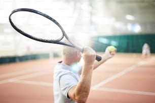 Tennis racket in held by mature professional player going to hit thrown ball with it