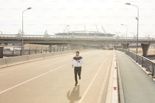 Young male runner jogging along racetrack along border during morning workout in urban environment