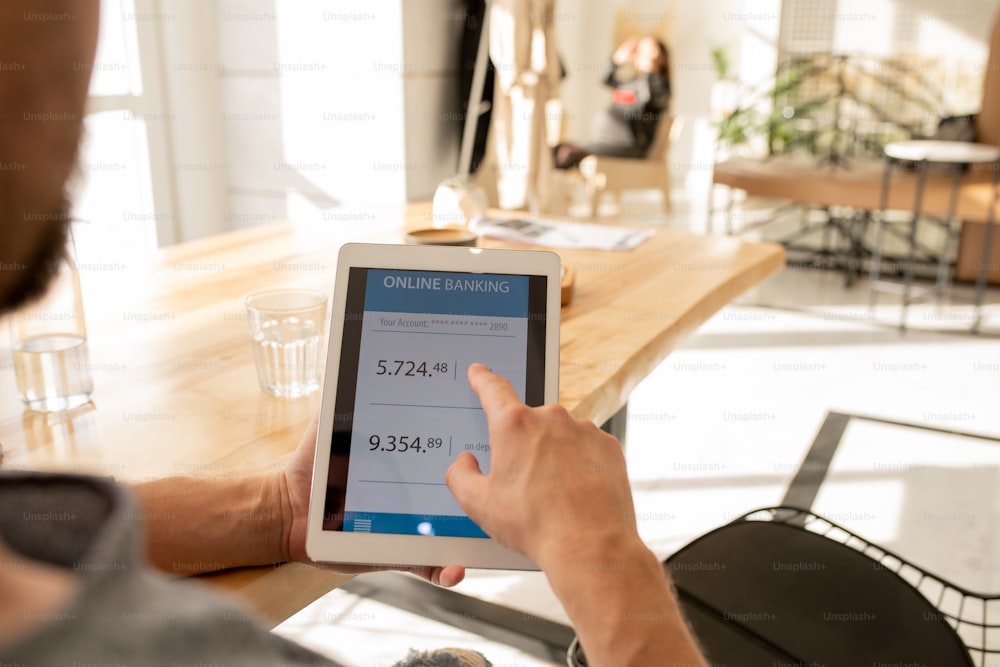 Young man pointing at financial information on touchpad display while checking his balance in personal bank