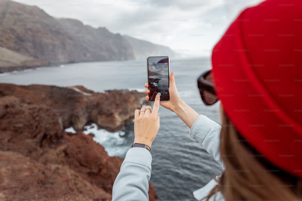 Mulher viajante fotografando no telefone vistas de tirar o fôlego sobre a costa rochosa do oceano enquanto viaja na ilha de Tenerife, Espanha