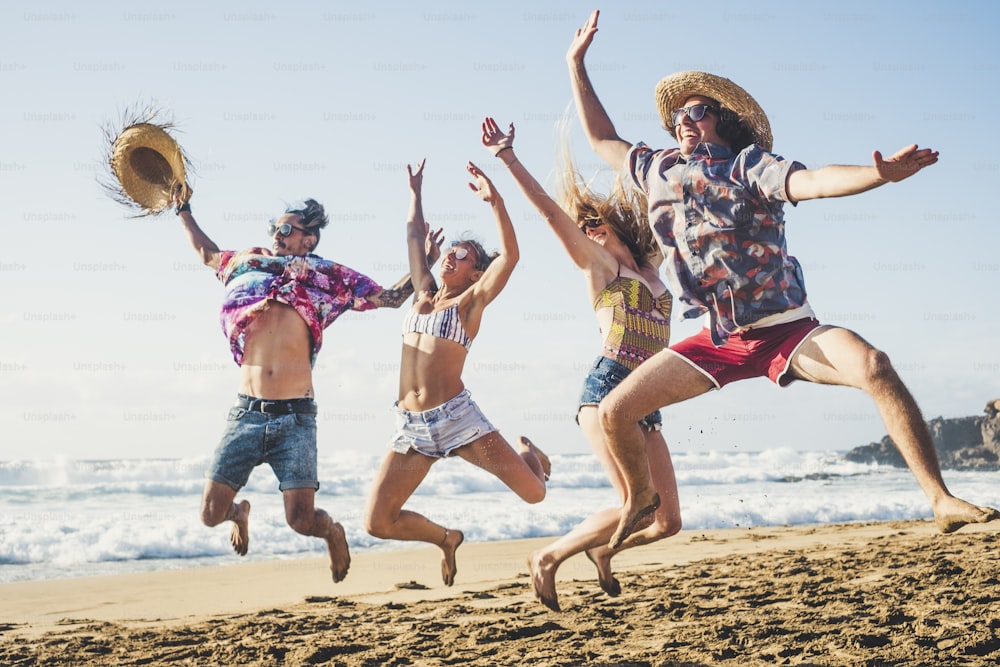 Felicidade e geração jovem pessoas se divertem juntos em amizade na praia para férias de verão pulando como louco e rindo muito com mar azul e céu ao fundo