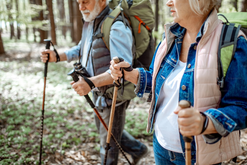 Senior man and woman hiking with trekking sticks in the forest, close-up view with cropped face