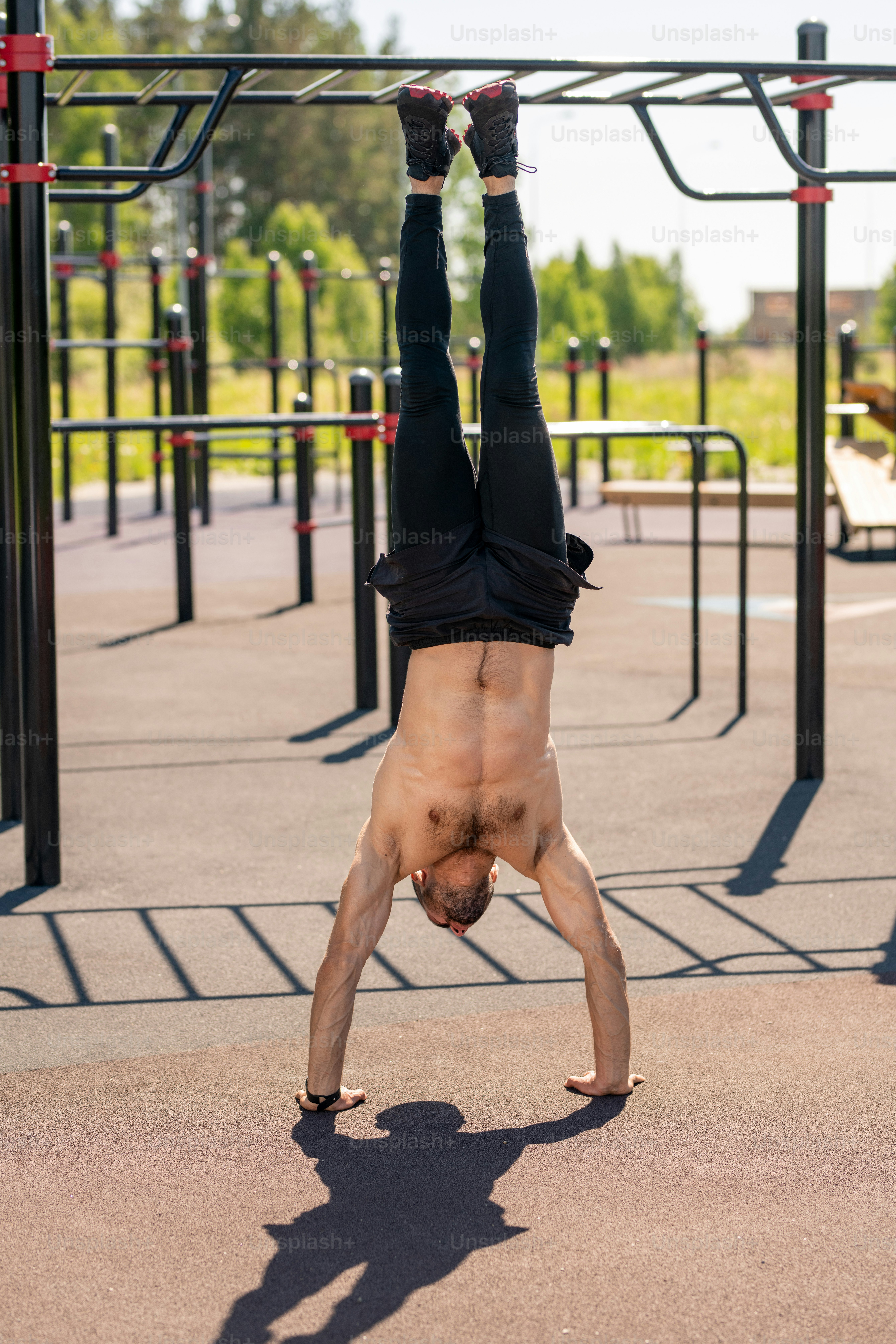 Front view of young shirtless muscular athlete doing handstand while exercising on sportsground