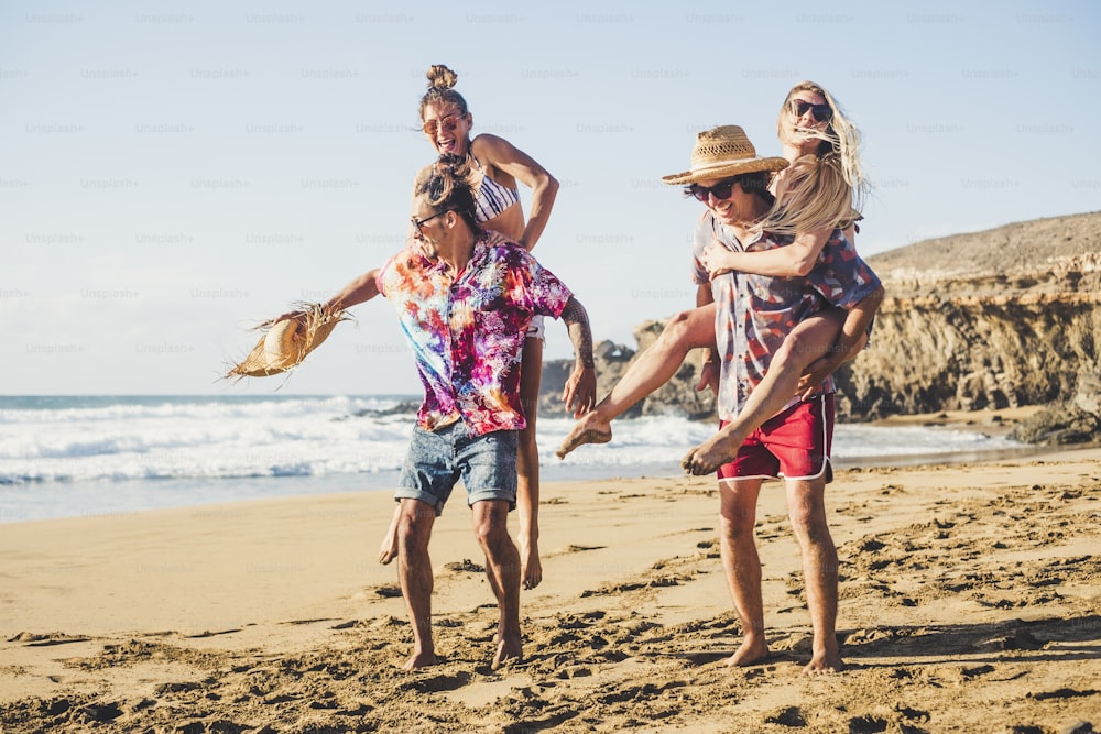 Happy group of people on vacation - youthful and funny concept with young men and women having fun together in friendship playing - boys carrying girls on their back - laugh and smile
